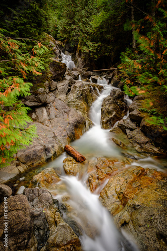 A waterfall flows over smooth rocks in a mountain forest with fall colors on the trees