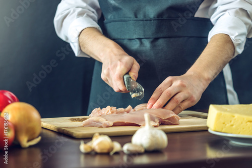 Zdjęcie XXL Szef kuchni w czarnym fartuszku wycina nożem filet z kurczaka. Koncepcja ekologicznych produktów do gotowania
