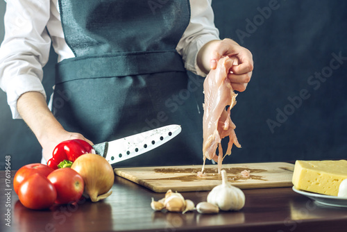 Plakat Szef kuchni w czarnym fartuszku wycina nożem filet z kurczaka. Koncepcja ekologicznych produktów do gotowania
