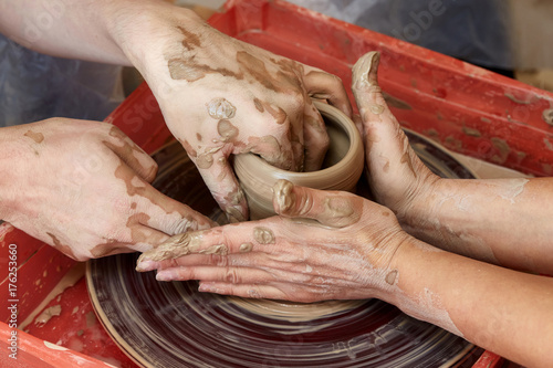 Hands of two people create pot, potter's wheel. Teaching pottery