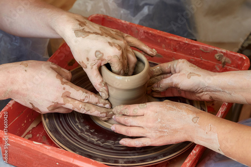 Hands of two people create pot, potter's wheel. Teaching pottery