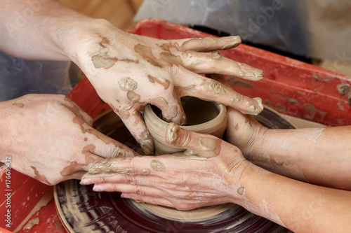 Hands of two people create pot, potter's wheel. Teaching pottery