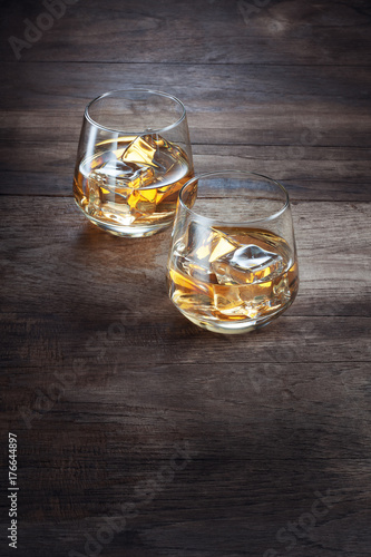 close up view of two glasses with ice and whiskey on wooden background