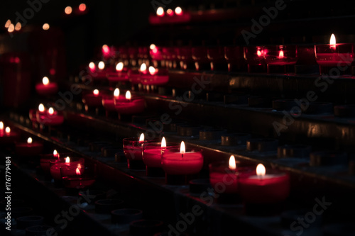 Rows of red candles inside a church. Candles lit as thoughts and prayers for loved ones. Lit candles inside a cathedral in Europe.