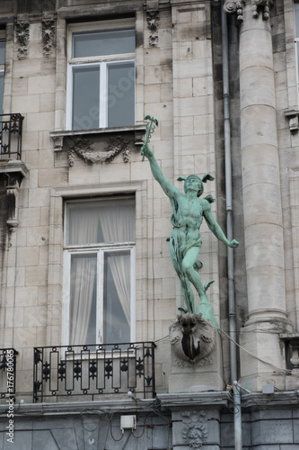 Statue of the Greek God Hermes (or Roman God Mercury) holding a caduceus, arm raised to the heavens on the side of a building in Antwerp, Belgium.