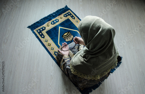 Plakat Muzułmańska kobieta modli się za Allaha muzułmańskiego boga przy izbowym pobliskim okno. Ręce muzułmańskiej kobiety na dywanie modląc się w tradycyjne stroje, Kobieta w Hidżab, dywan z Kaaba, Selektywne focus