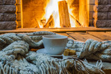 Cup of tea and sugar, woolen things near cozy fireplace, in country house, winter vacation, horizontal.