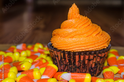 Plakat Pomarańczowy buttercream frosting na bogatej czekoladowej ciasteczce, otoczony słodyczami cukierków kukurydzianych. Halloweenowy jesień temat dla świętowania lub przyjęcia.