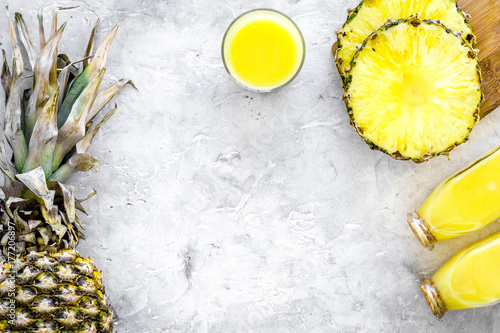 Non-alcoholic beverages. Bottle with fruit juice near pineapples slices on grey background top view copyspace