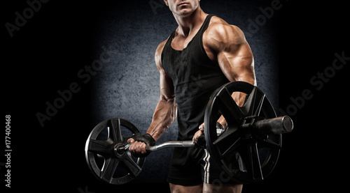 Plakat Młody seksowny bodybuilder z perfect ciałem robi ćwiczeniu z barbell na czarnym tle.