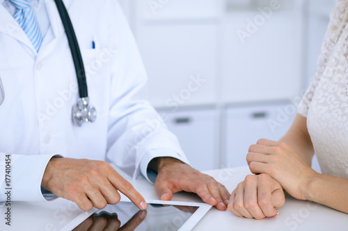 Plakat Doktorski i cierpliwy opowiadać podczas gdy siedzący przy biurkiem w biurze. Lekarz wskazując na komputer touch pad lub tabletu. Medycyna i koncepcja opieki zdrowotnej