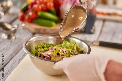 Fotoobraz na płótnie Szef kuchni wylewa sos na mieszaną sałatkę. Zielona zdrowa sałatka w nierdzewnym pucharze w restauraci. Szef kuchni gotowania danie w kuchni restauracji.