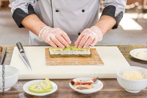 Fotoobraz na płótnie Szef kuchni przygotowuje sushi z węgorza i awokado. Szef kuchni ręce w rękawice jednorazowe gotowania sushi w kuchni japońskiej restauracji.