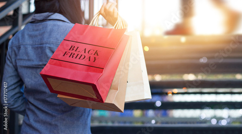 Rear view of woman holding Black Friday shopping bags while on up stairs outdoors mall background