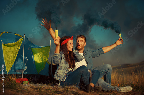 Young happy couple holding smoke bombs on camping