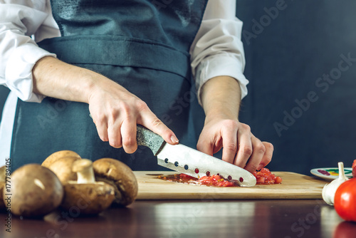 Plakat Szef kuchni w czarnym fartuchu pokroił pomidory. Koncepcja ekologicznych produktów do gotowania
