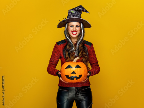 smiling young woman showing jack-o-lantern pumpkin