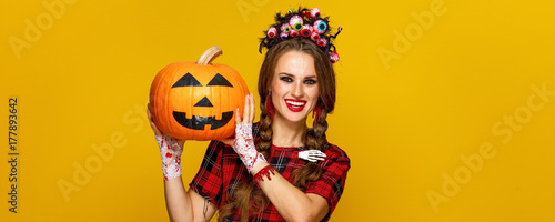 smiling young woman showing jack-o-lantern pumpkin