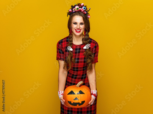 happy woman on yellow background holding jack-o-lantern pumpkin