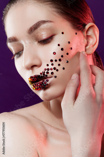 Young beautiful girl with blue eyes. Bright makeup, red lipstick. Art, rhinestones on the lips and face