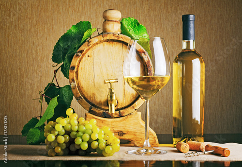 Fotoobraz na płótnie Drewniana beczka na wino z gałązką winogronową. Butelka białego wina