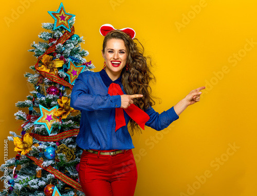 happy stylish woman near Christmas tree pointing at something