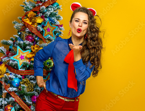 smiling young woman near Christmas tree blowing air kiss