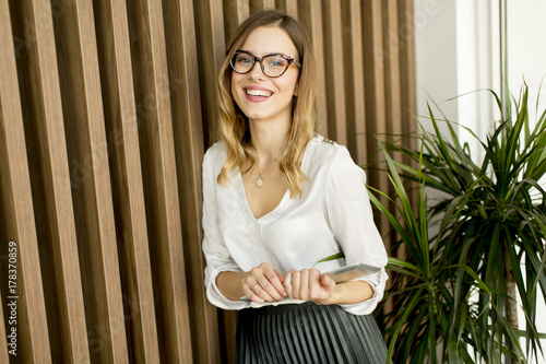 Young businesswoman with tablet by wall in modern office