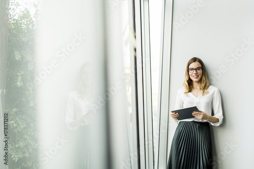 Young businesswoman standing wirth tablet in the office by window