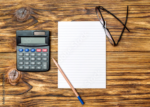 Office table with stationery. Blank notepad with calculator and glasses on the desk. Top view. Business concept.