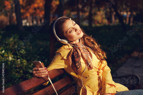 Young woman enjoys music through the headphones in the park