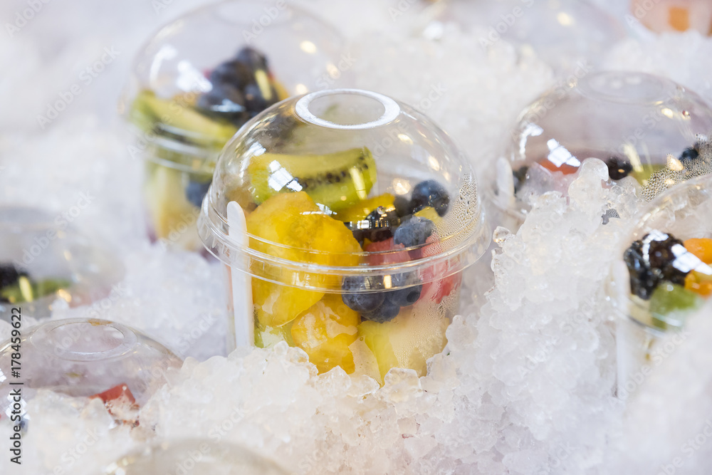 Fresh fruit in plastic cups on a showcase with ice.