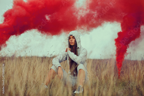 Portrait of a young woman in a meadow with smoke bomb in the background
