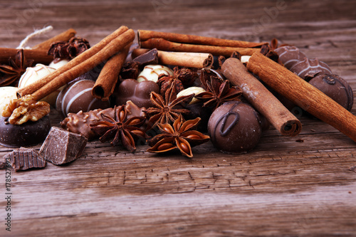 A selection of assorted chocolate truffle pralines on a wooden table with dark chocolate, cinnamon and anise.