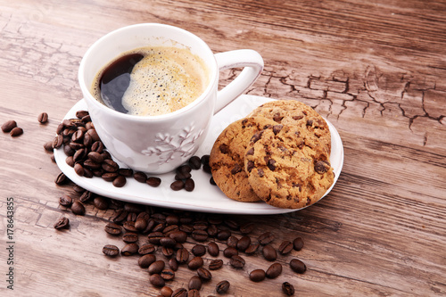 Coffee cup with chocolate cookies and coffee beans on wooden background