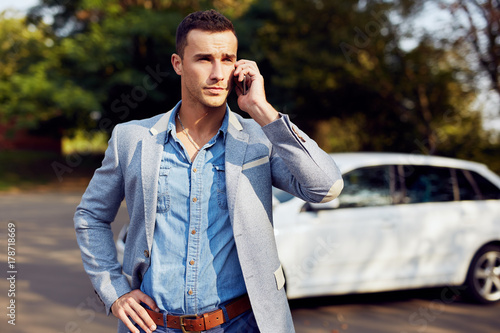 Portrait of a man standing at a white car and calling