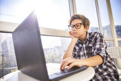 Teen boy using laptop by window
