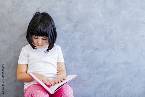 Cute black hair little girl reading book by the wall