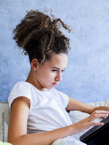 Curly hair girl using digital tablet on sofa