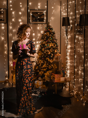 portrait of beautiful young sexy curly red-haired girl on background merry christmas happy new year tree lights with star gift decor