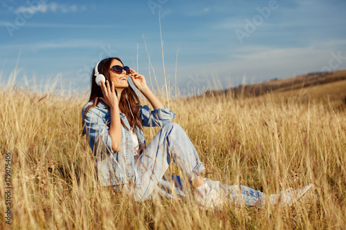 Young woman listens to music and sitting  in the meadow