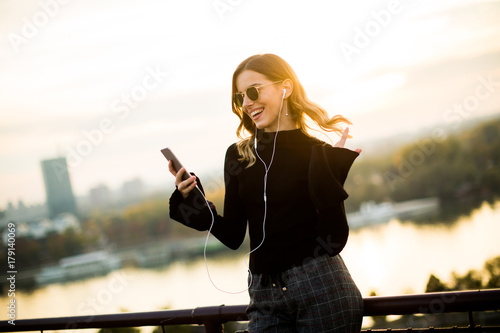 Trendy woman listening music from smartphone outdoor at sunset