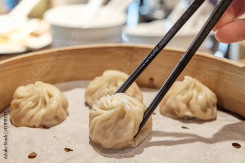 Soup dumplings in a bamboo steam basket being picked up by chopsticks