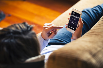 Woman listening podcast in a mobile phone while lies down on a sofa at home.