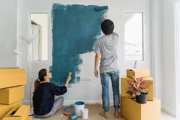 Young asian couple painting interior wall with paint roller in new house