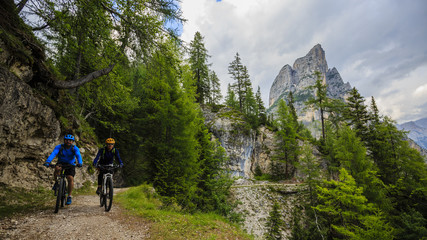 Tourist cycling in Cortina d'Ampezzo, stunning rocky mountains on the background. Family riding MTB enduro flow trail. South Tyrol province of Italy, Dolomites.