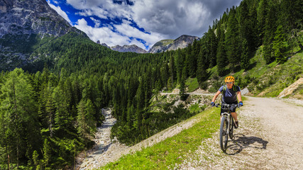 Tourist cycling in Cortina d'Ampezzo, stunning rocky mountains on the background. Family riding MTB enduro flow trail. South Tyrol province of Italy, Dolomites.