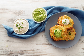 vegetable rosti from cauliflower and parmesan with two dips from sour cream and avocado, parsley garnish, blue plate and napkin on a bright wooden table with copy space, high angle view from above