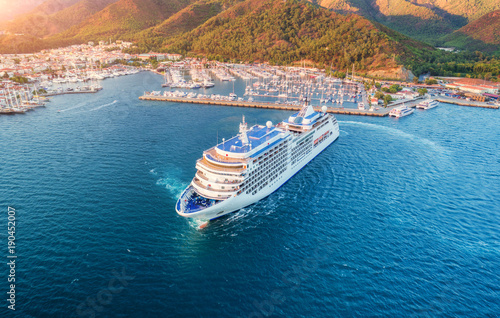 Cruise ship at harbor. Aerial view of beautiful large white ship at sunset. Colorful landscape with boats in marina bay, sea, green forest. Top view from drone of yacht. Luxury cruise. Floating liner © den-belitsky