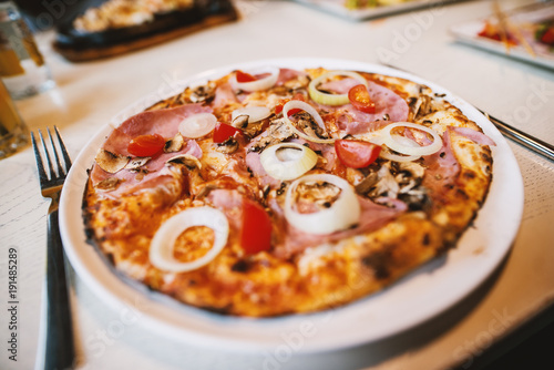 Plakat Wyśmienicie pizza z pomidorem i cebulą na białym talerzu przy restauracją podczas gdy przyjaciele ma lunch.